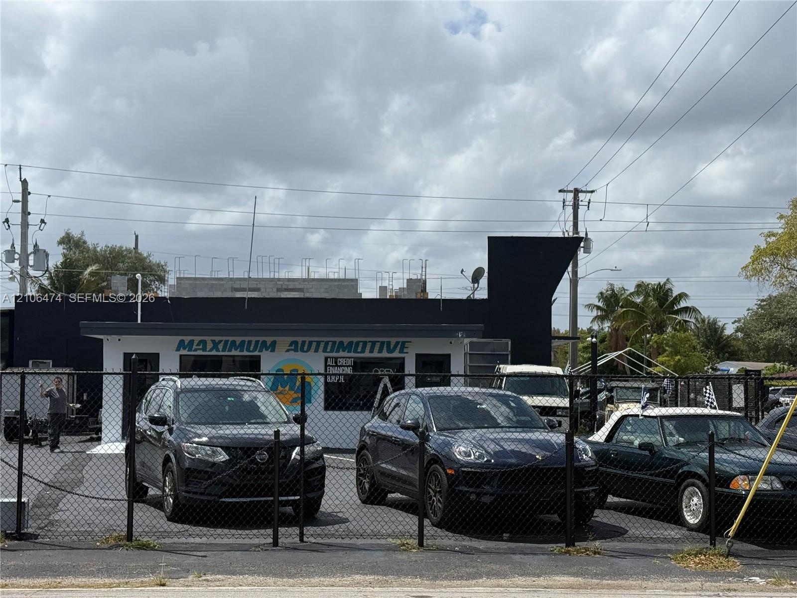 Commercial structure featuring a flat roofline, dark-toned exterior finish, and a paved lot secured by chain-link fencing
