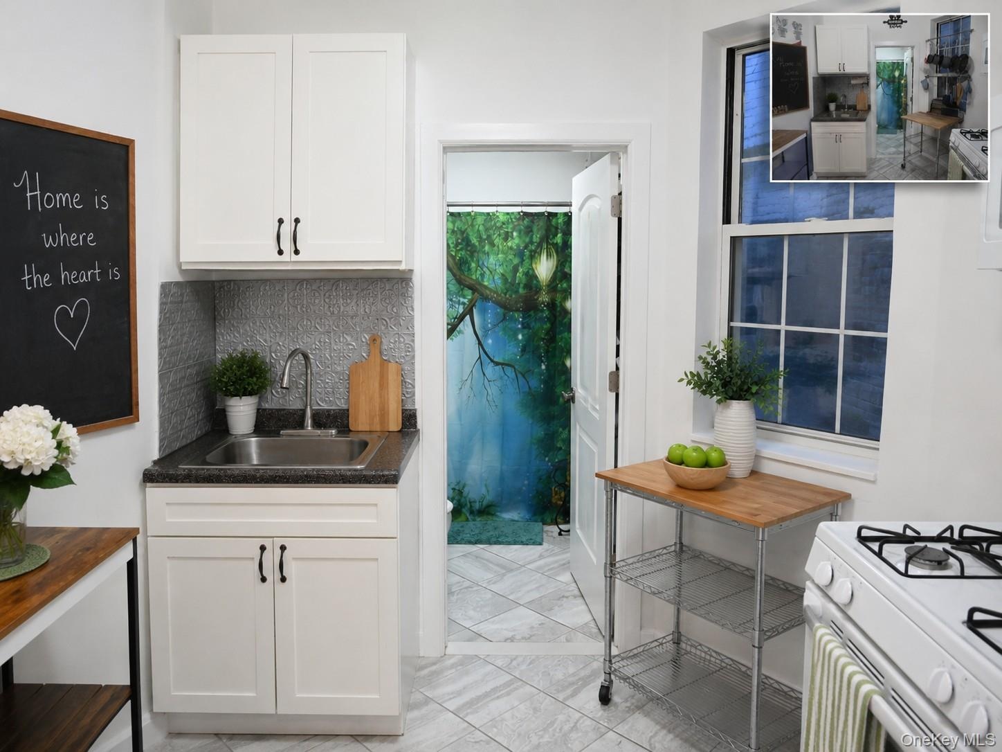 Compact kitchen featuring white cabinetry, a stainless steel sink, and a textured backsplash (virtually staged)