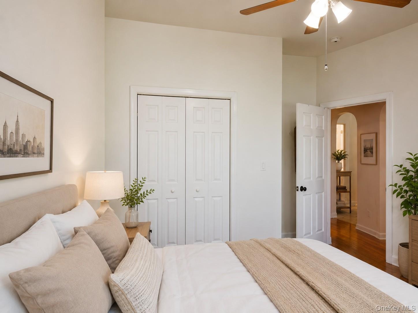 Bedroom featuring a ceiling fan with integrated lighting, wood-finish flooring, and white bi-fold closet doors (virtually staged)