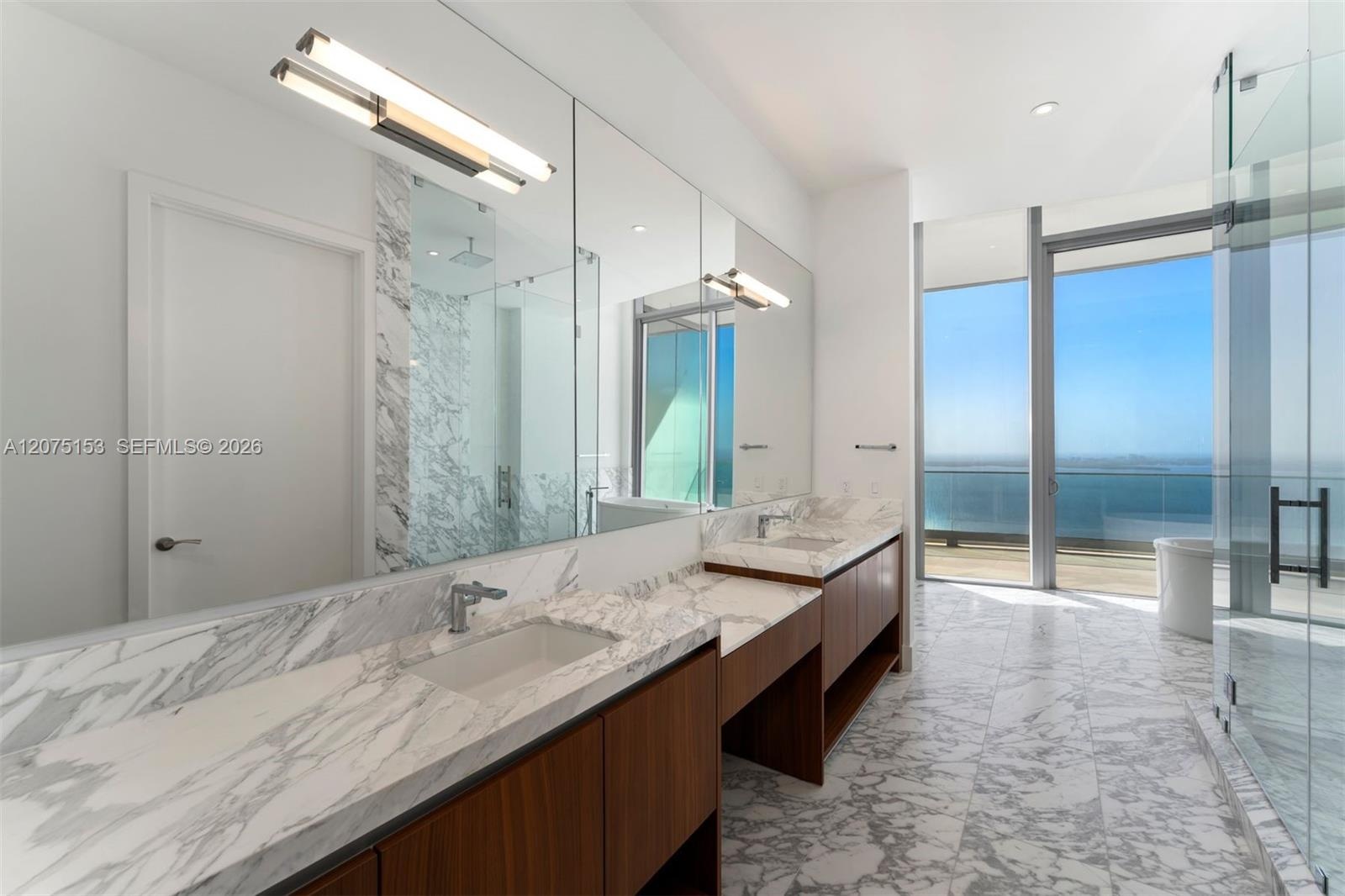 Bathroom featuring dual-sink vanity with stone-surfaced countertop, full-height wall mirror, recessed lighting, and floor-to-ceiling windows