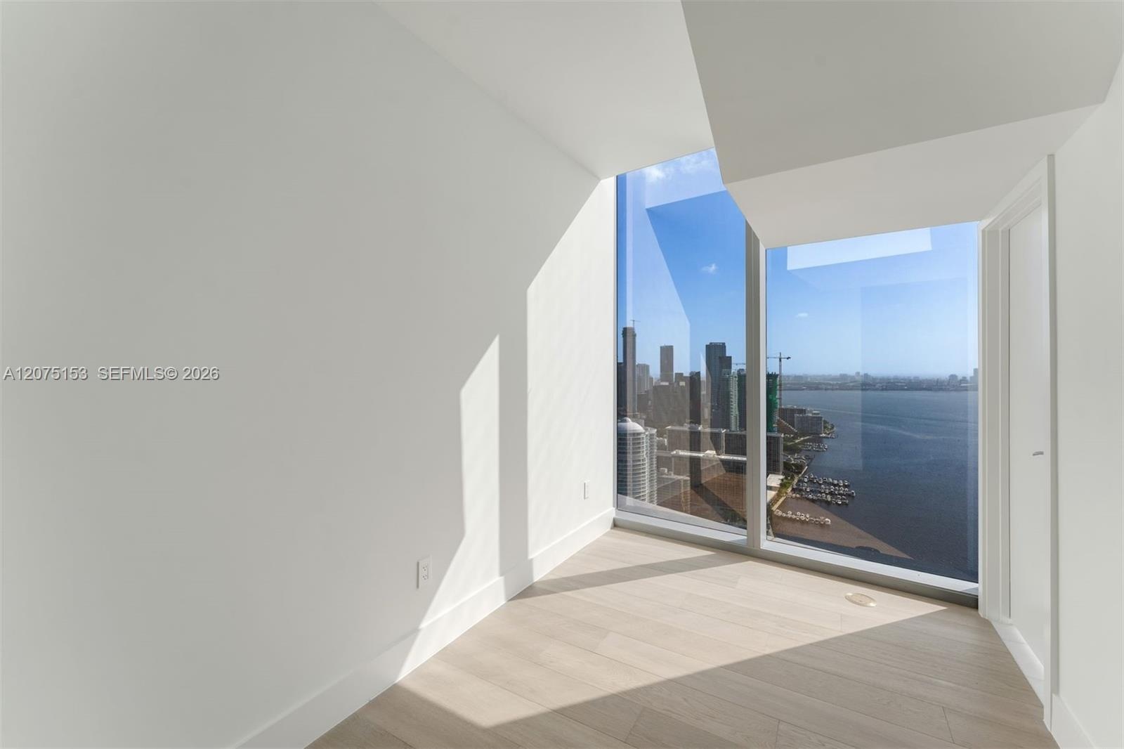 Floor-to-ceiling windows featuring panoramic urban and waterfront scenery, light-toned wood-finish flooring, and minimalist white walls