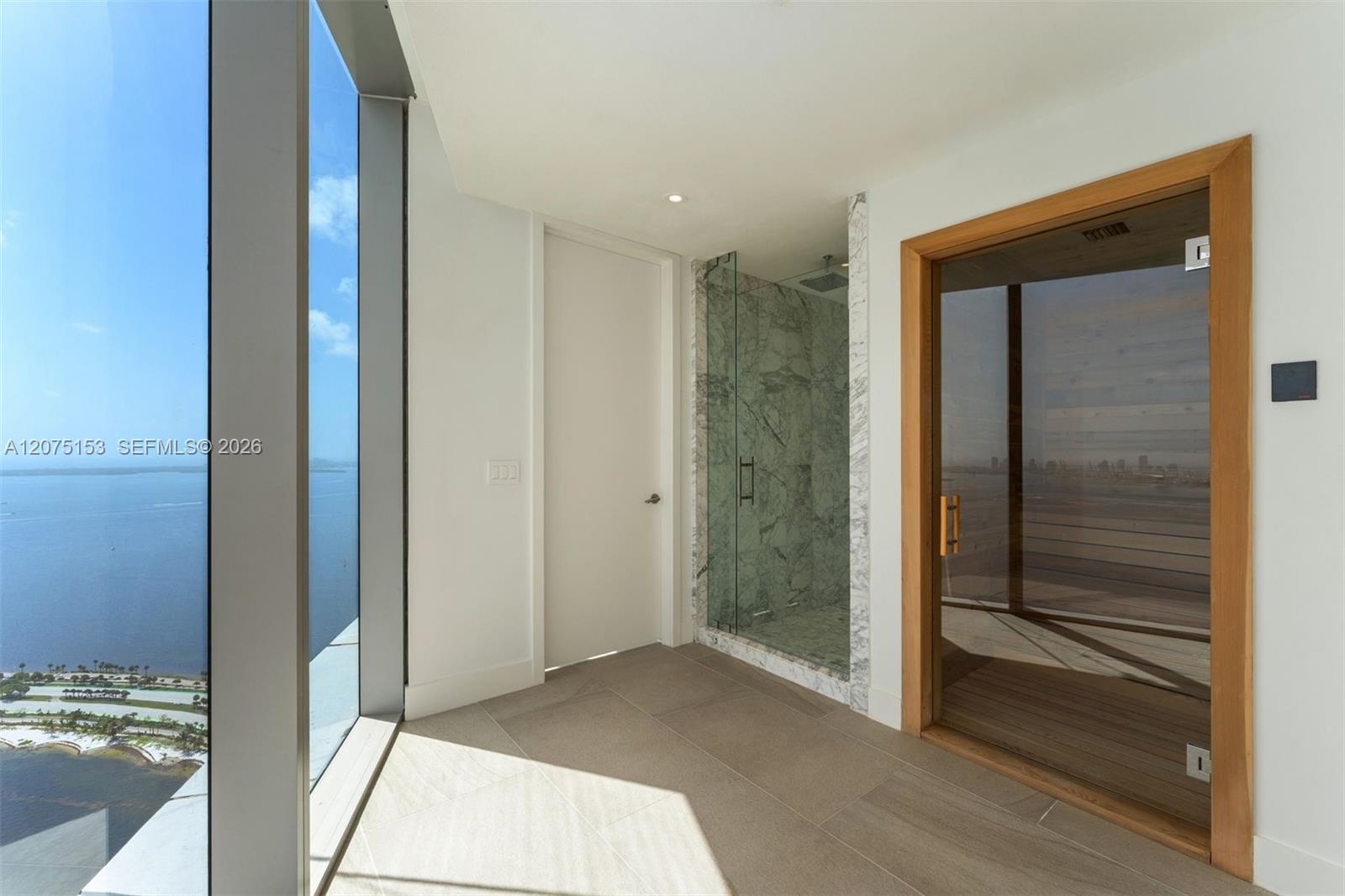 Floor-to-ceiling windows, integrated sauna with glass door and wood-finish interior, walk-in shower with stone-surround, and neutral large-format tile