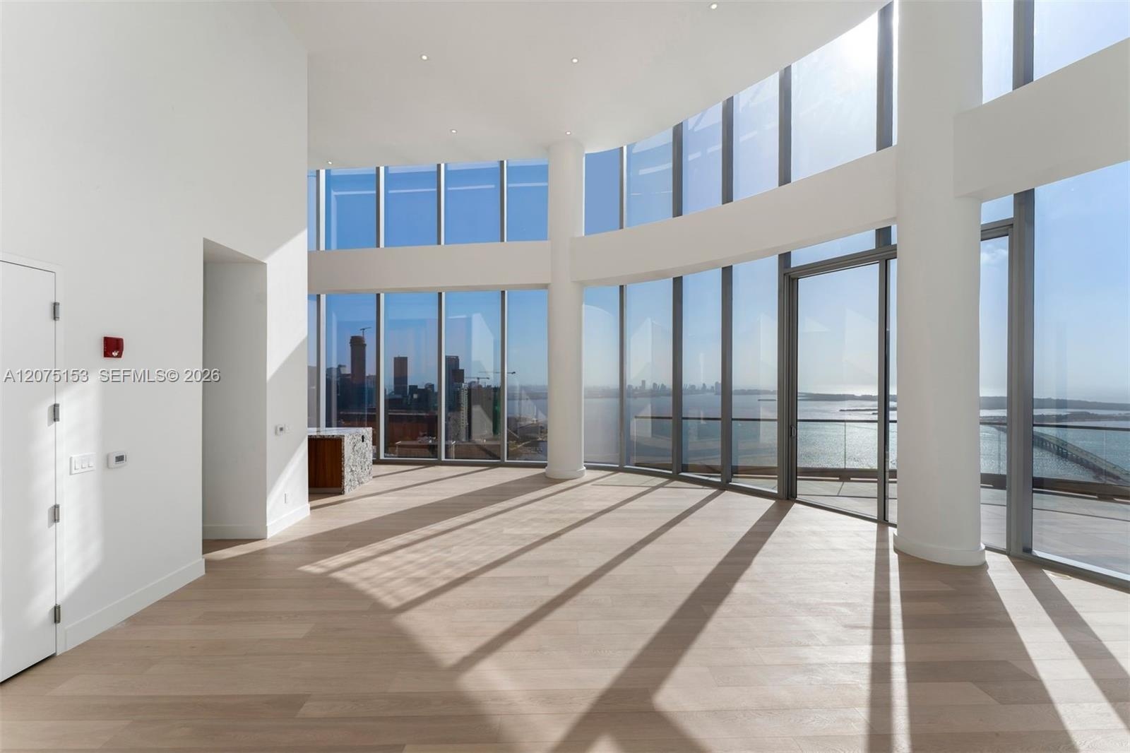 Curved floor-to-ceiling glass curtain wall, wood-finish flooring, recessed ceiling lighting, and structural cylindrical columns