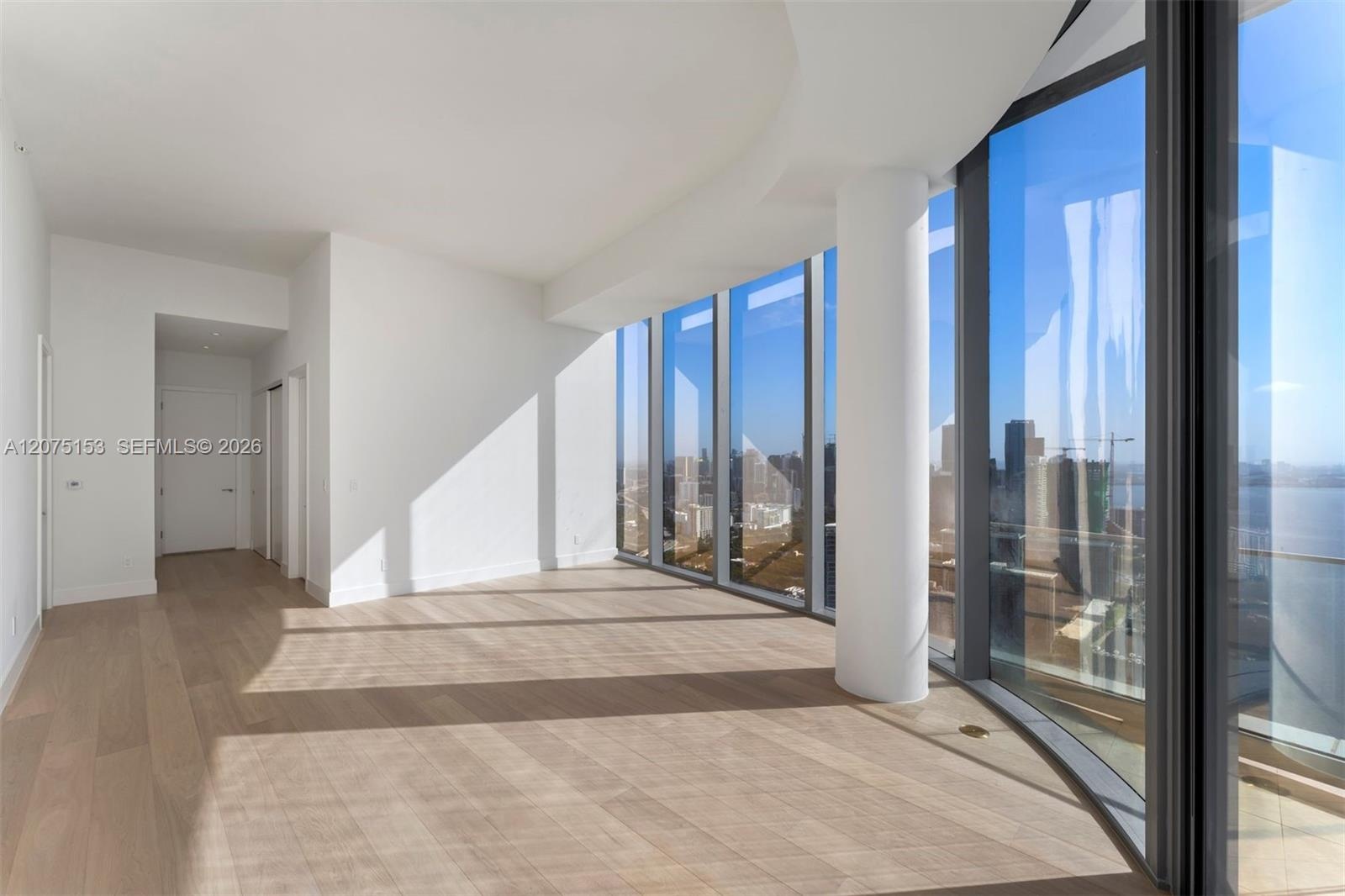 Floor-to-ceiling glass curtain walls, expansive wood-finish flooring, structural cylindrical column, and minimalist white interior finish