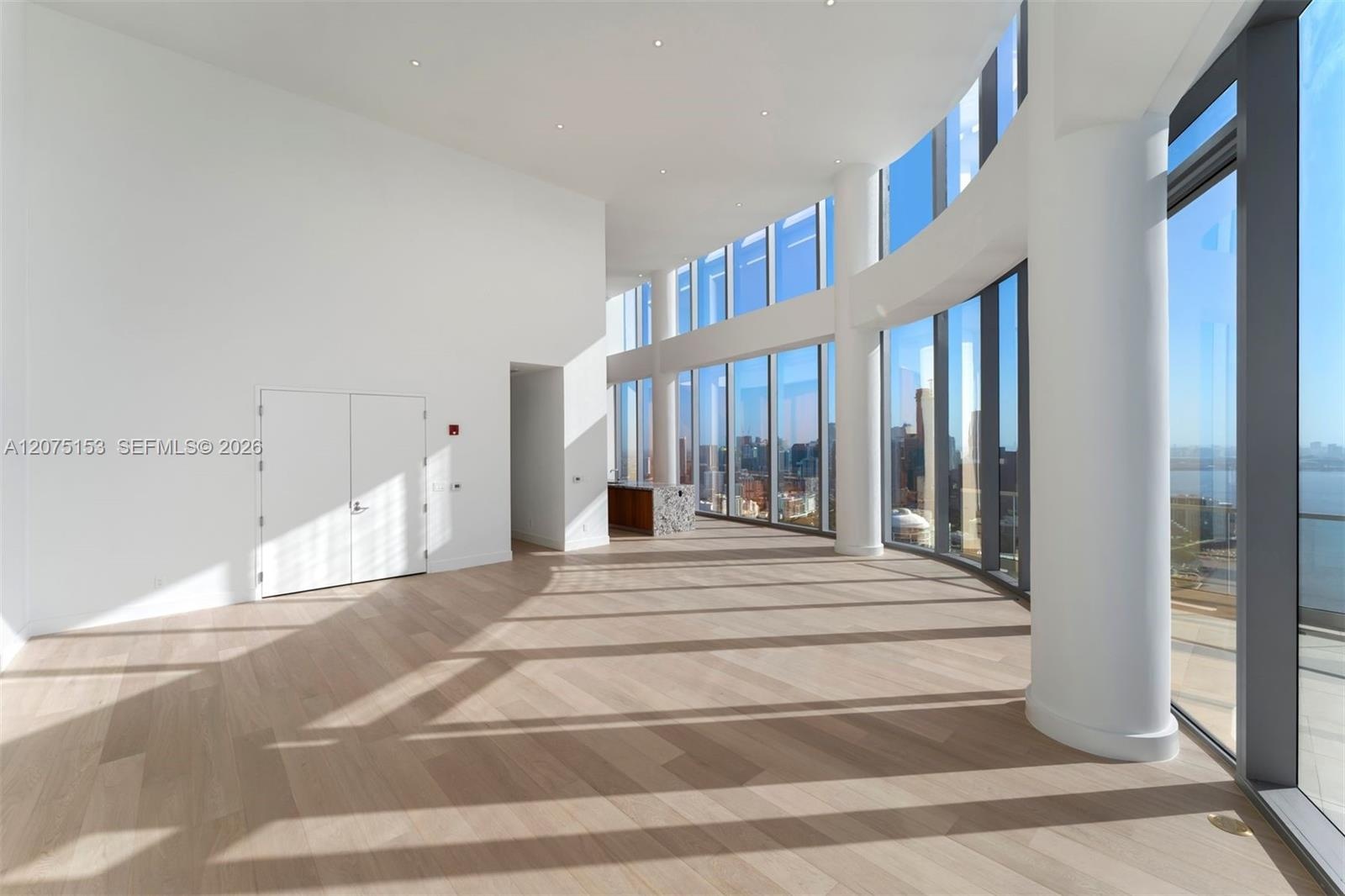 Open-concept interior featuring floor-to-ceiling curved glass windows, wood-finish flooring, recessed lighting, and structural columns