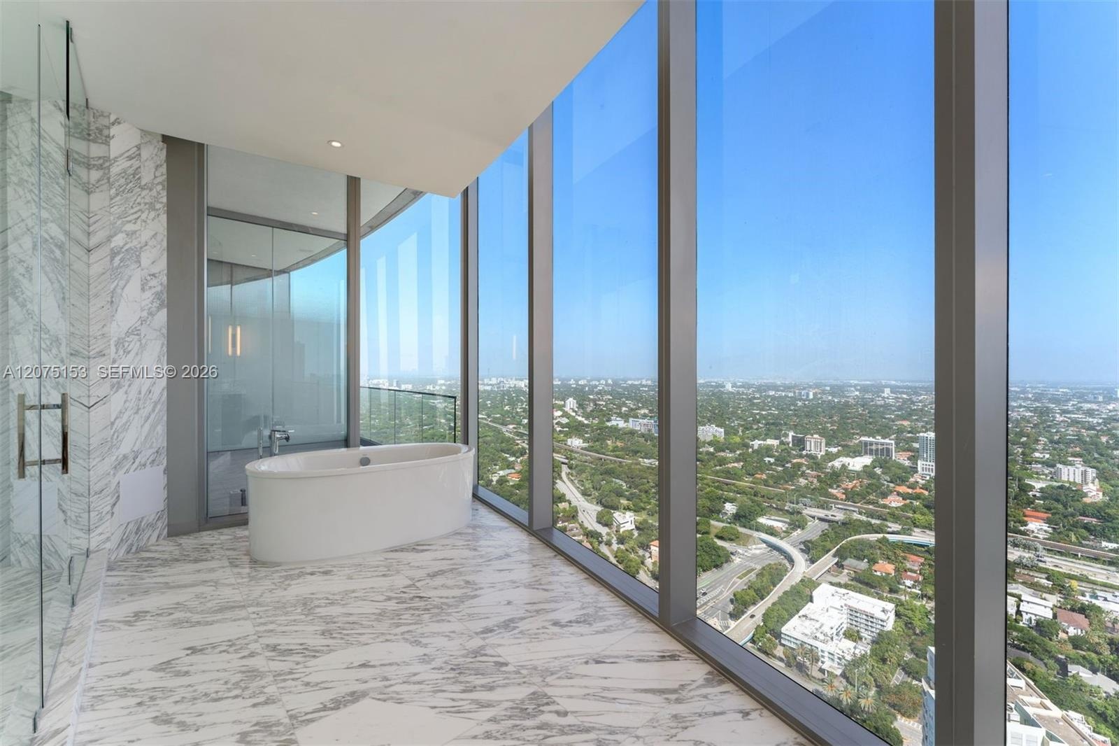 Floor-to-ceiling windows, freestanding soaking tub, stone-finish wall cladding, stone-finish flooring, and glass-enclosed shower