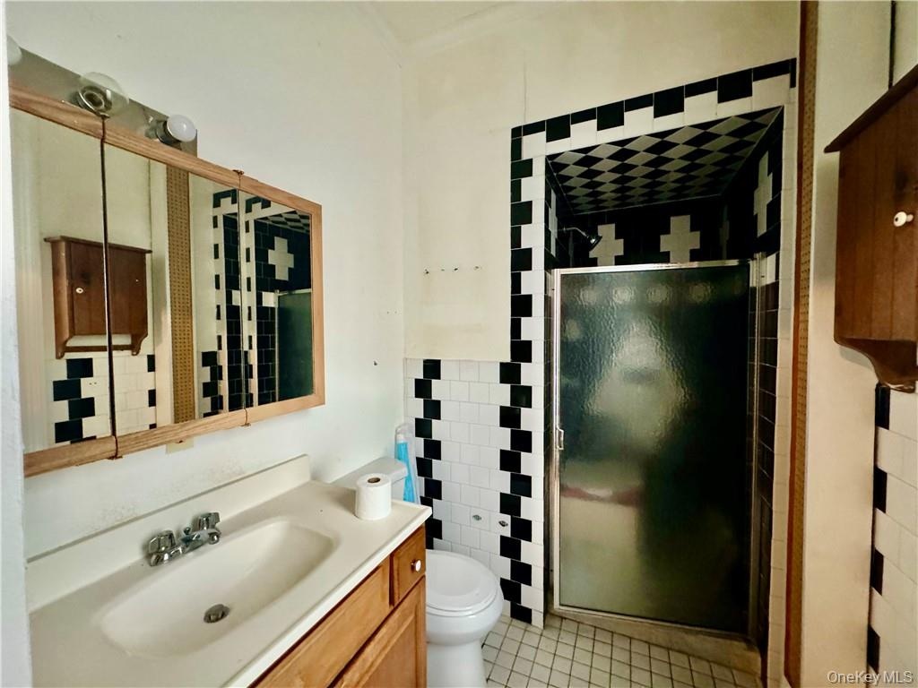 Bathroom featuring a shower with shower door, toilet, tile patterned floors, tile walls, and vanity