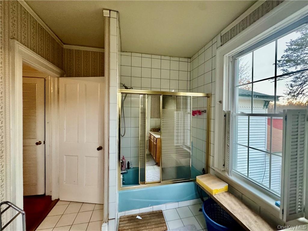 Bathroom with tile patterned floors, combined bath / shower with glass door, and ornamental molding