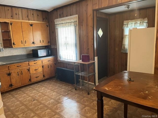 Kitchen featuring freestanding refrigerator, wood walls, dark countertops, brown cabinets, and open shelves