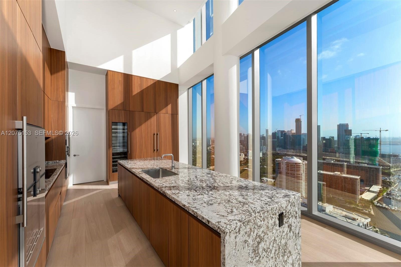 Gourmet kitchen featuring floor-to-ceiling cabinetry, stone waterfall island, integrated stainless steel appliances, and expansive double-height windo