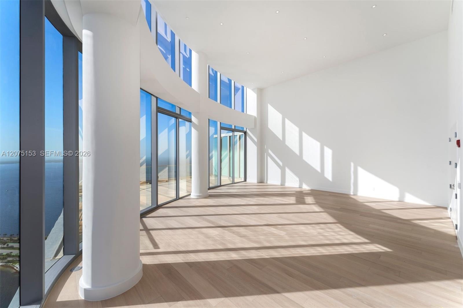 Floor-to-ceiling glass walls, curved architectural columns, double-height ceilings, recessed lighting, and wood-finish flooring