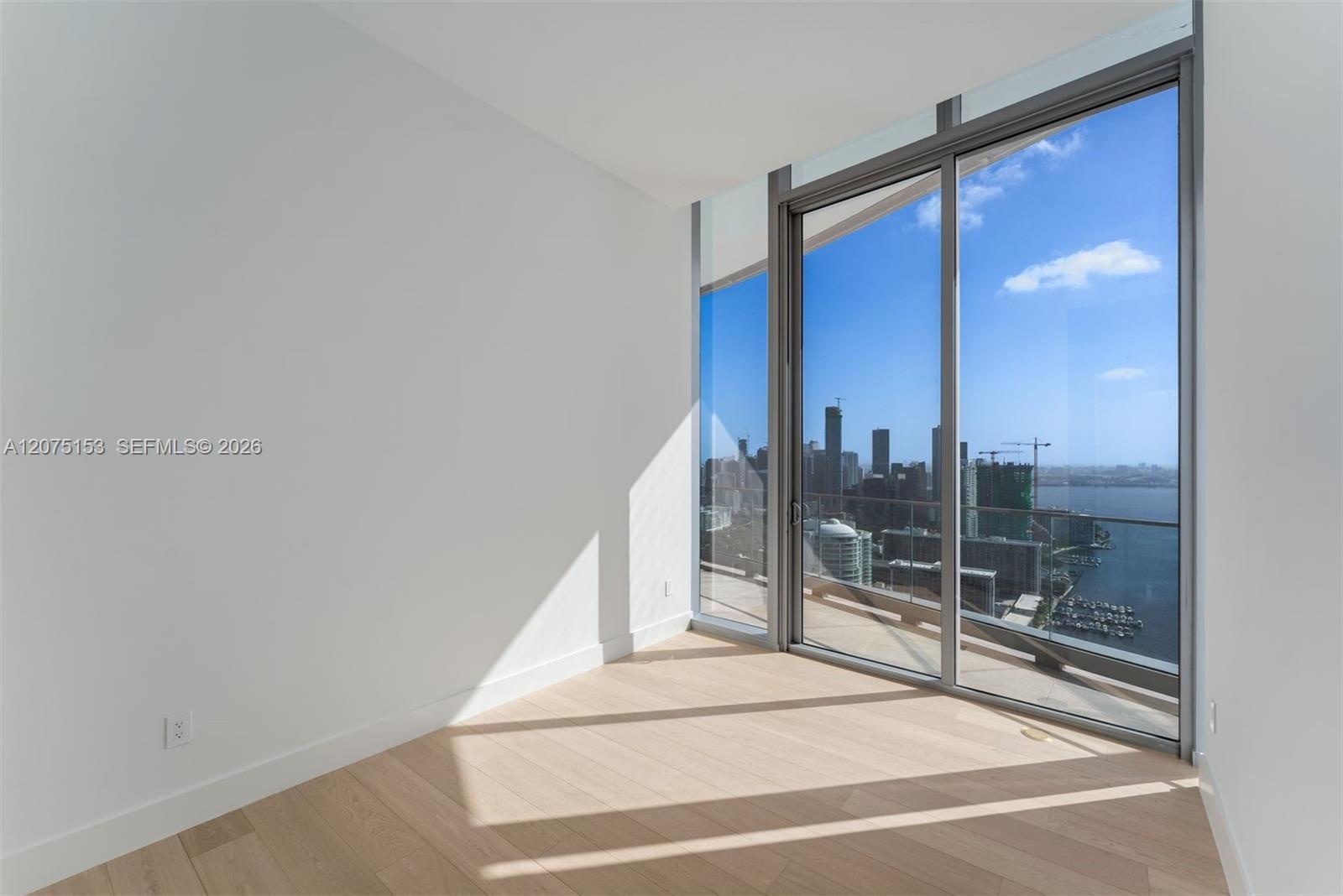 Floor-to-ceiling glass corner windows, wood-finish flooring, and a private glass-railed balcony with expansive urban and water scenery