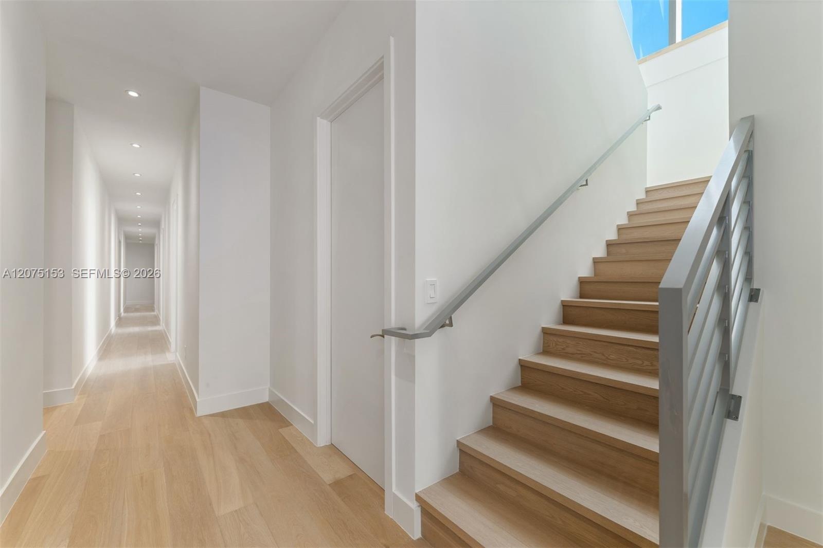 Staircase featuring wood-finish treads, metal handrails, and vertical metal balusters, complemented by recessed ceiling lighting and wood-finish floor