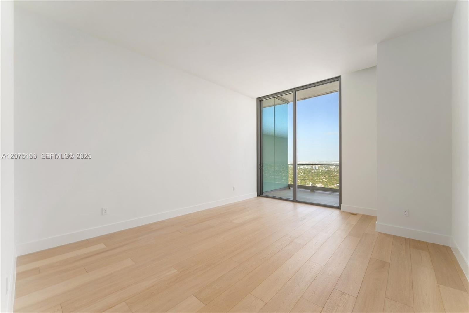 Floor-to-ceiling glass sliding door, wood-finish flooring, and white walls featuring exterior balcony access