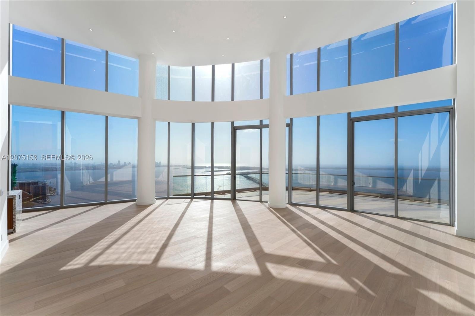 Curved wall of floor-to-ceiling windows, wood-finish flooring, recessed ceiling lighting, and structural support columns