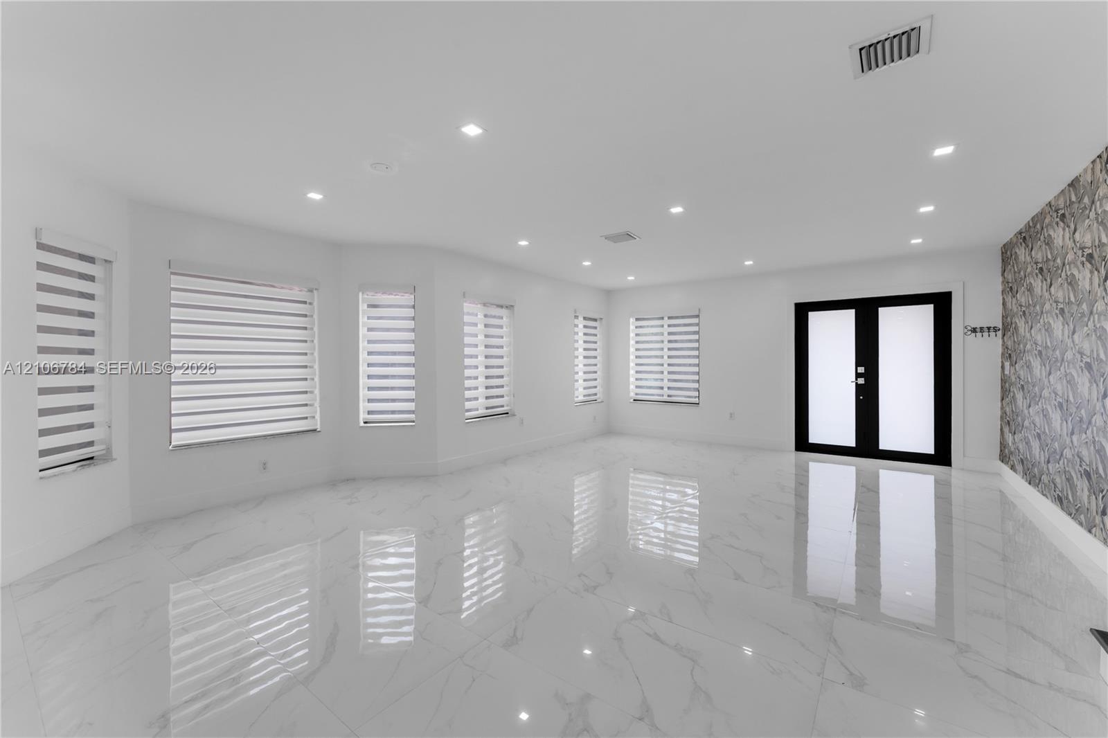 Open-concept area featuring polished porcelain tile flooring, recessed lighting, textured stone accent wall, dual-entry doors with frosted glass panel
