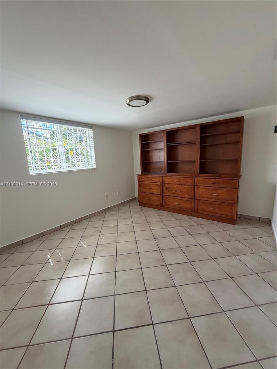 Built-in wooden cabinetry featuring open shelving and integrated drawers, ceramic tile flooring, and a window with security grating