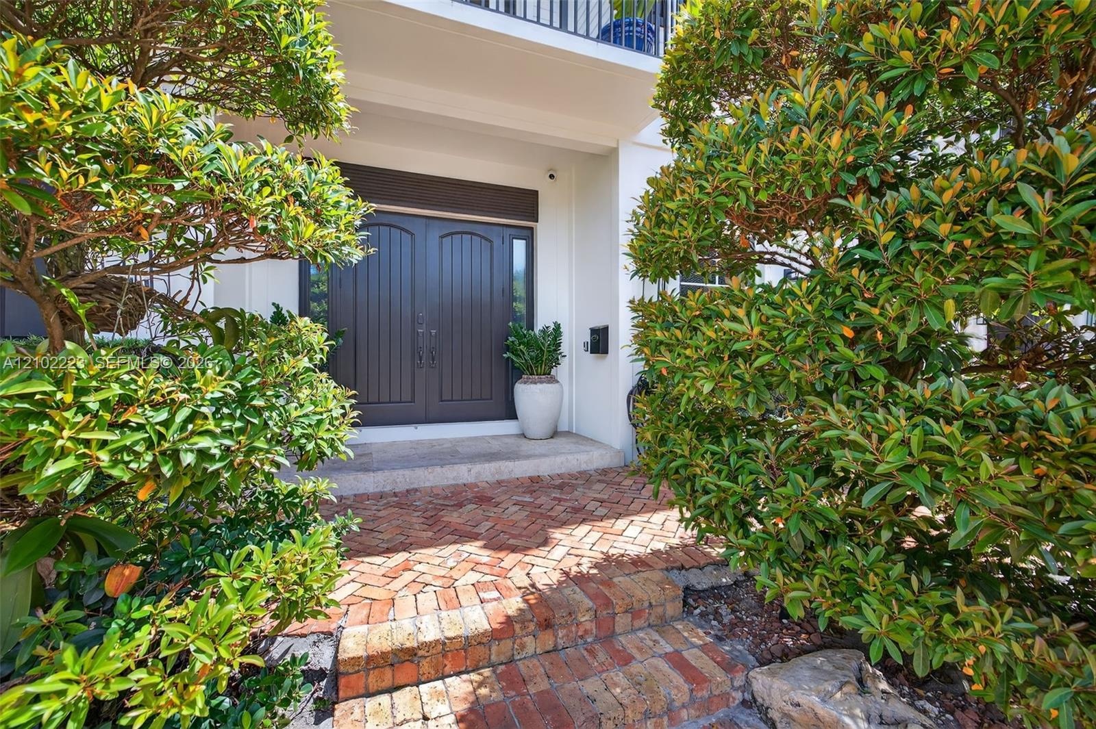 A distinguished entrance framed by lush Tropical Landscaping with beautiful brick paver steps lead to an elegant, natural stone, Landing and impressiv