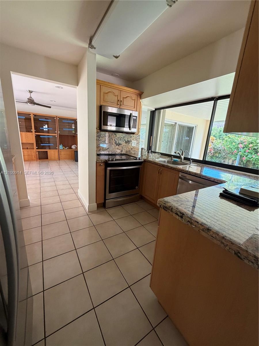 Kitchen featuring wood cabinetry, stone-finish countertops, stainless steel appliances, tile flooring, and a large window
