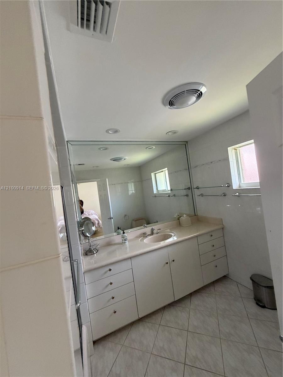 Bathroom vanity featuring solid-surface countertop with an integrated basin, white cabinetry, expansive wall-to-wall mirror, polished metal fixtures, 