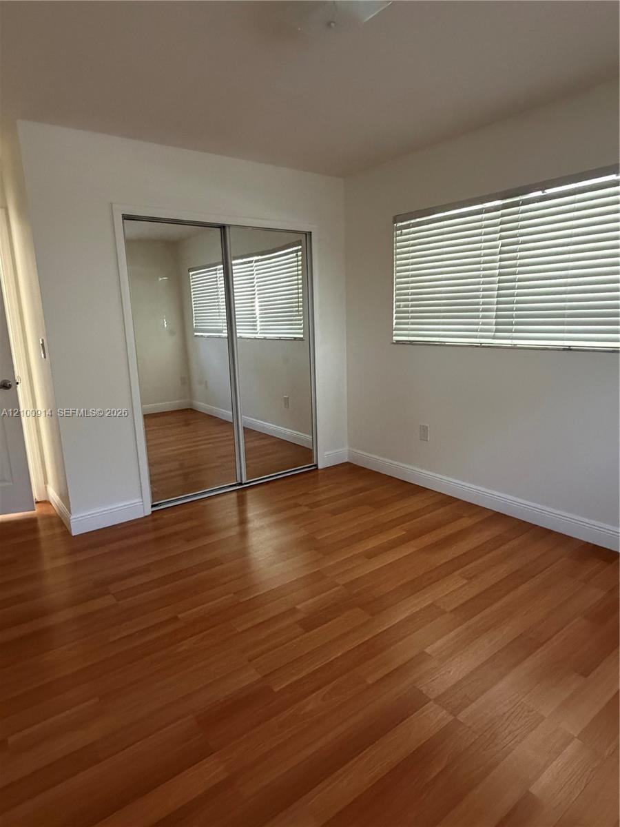 Room featuring wood-finish flooring, mirrored sliding closet doors, and windows with horizontal blinds