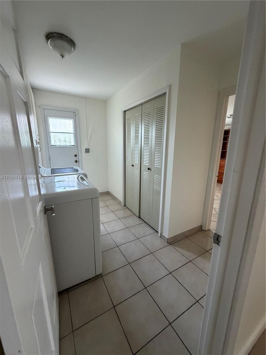Utility room featuring ceramic tile flooring, dual-panel louvered closet doors, and an exterior door with integrated window