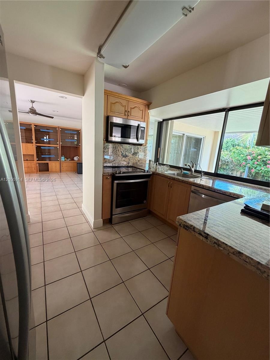 Kitchen featuring wood cabinetry, stone countertops, stainless steel appliances, ceramic tile flooring, and a large window