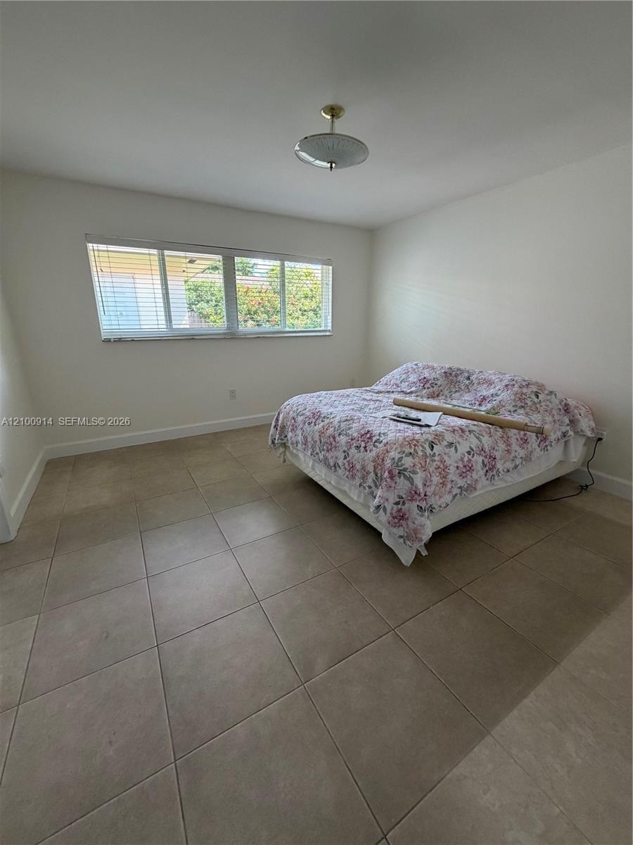 Neutral interior space featuring large-format ceramic tile flooring, horizontal window blinds, and a central semi-flush mount light fixture