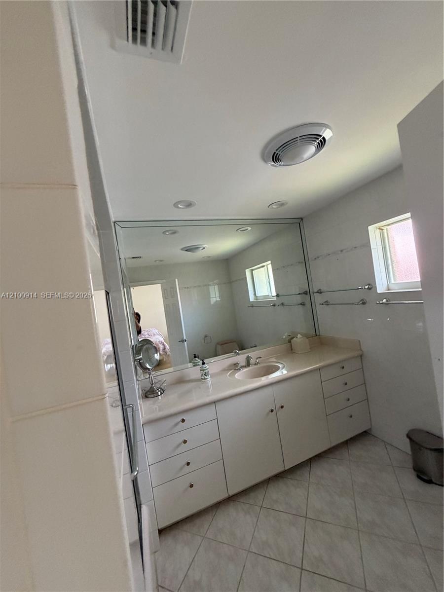 Bathroom featuring a solid-surface vanity with an integrated sink, expansive wall-to-wall mirror, neutral tile flooring, and metallic wall-mounted tow