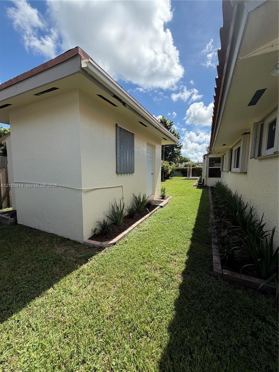Exterior side yard featuring stucco finish, dedicated storage structure, manicured lawn, and defined landscape beds
