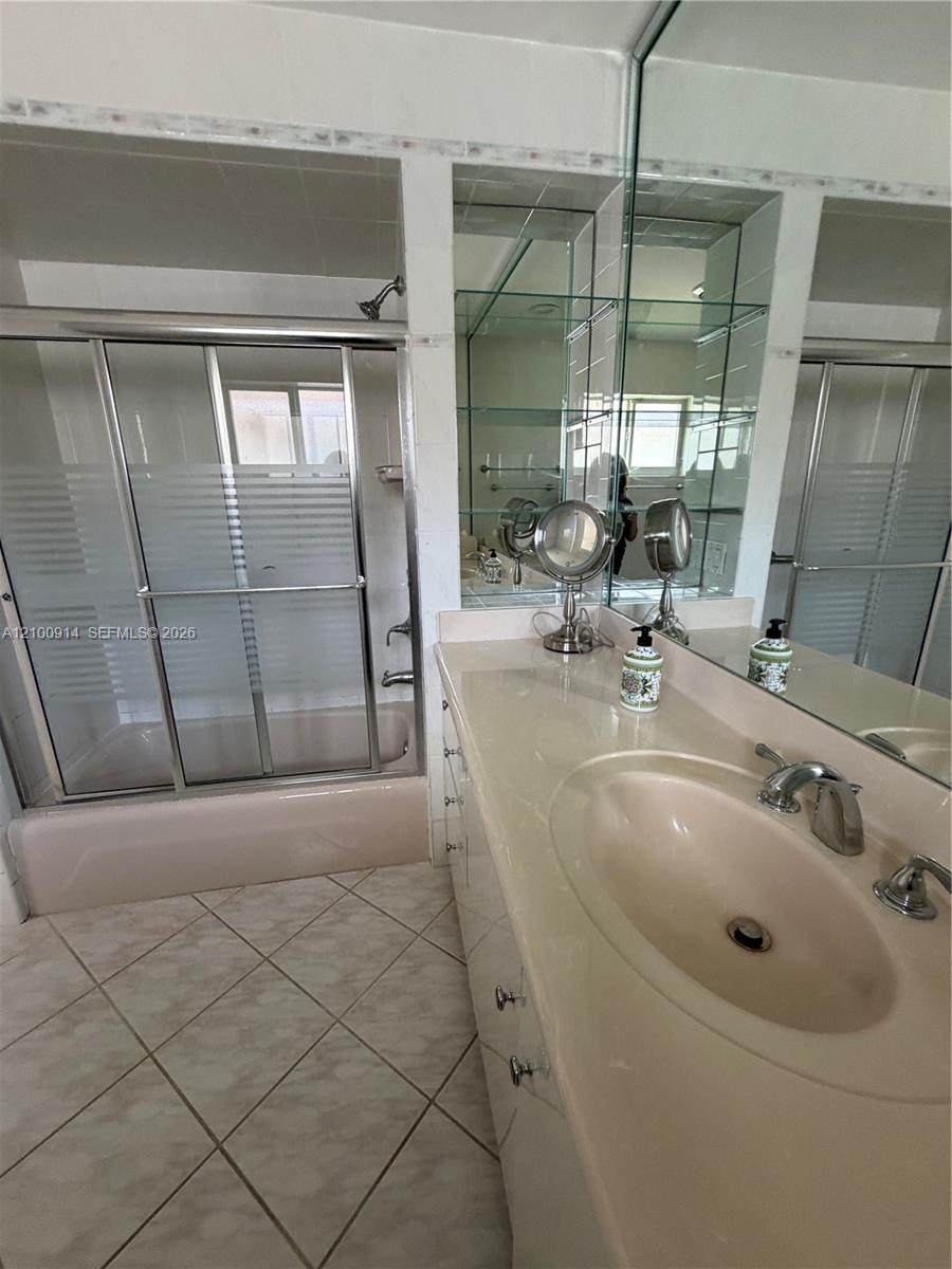 Vanity with a solid-surface countertop and integrated sink, full-width mirror, tile flooring, and a shower-tub combination with a sliding glass door