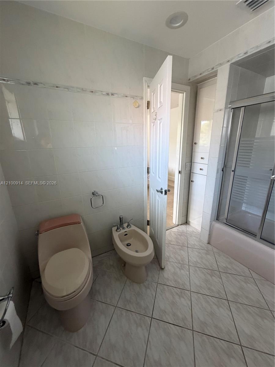 Bathroom featuring neutral tile wall wainscoting with decorative accent trim, floor-to-ceiling built-in cabinetry, and a shower-tub combination with a