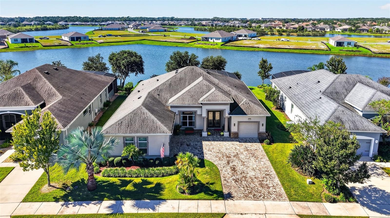 An aerial drone view highlights the front exterior of the home, framed by a serene lake backdrop.