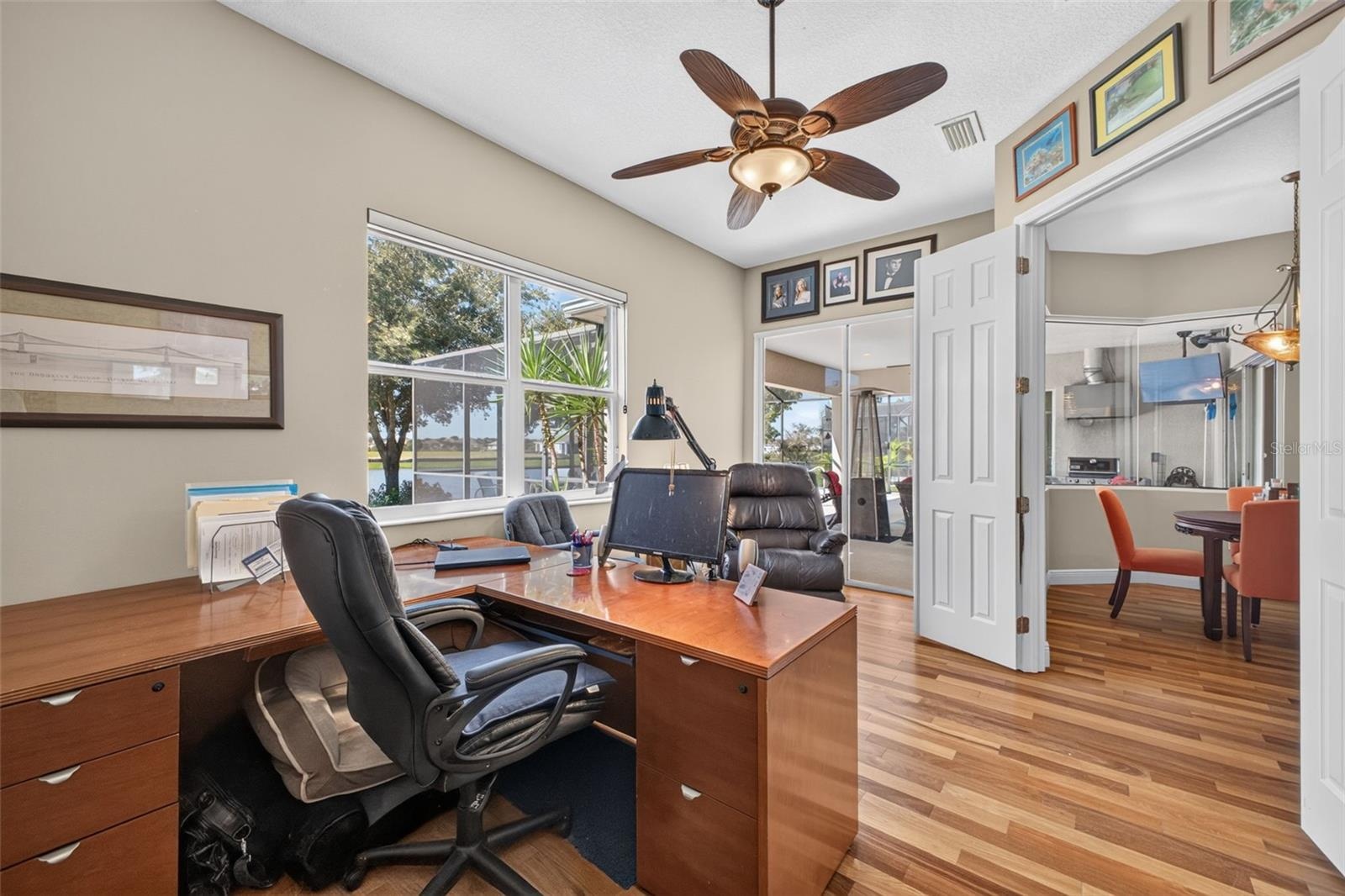 Framed by serene lake views, this dedicated home office features sliding glass doors that step directly out onto the lanai for an inspiring indoor-out