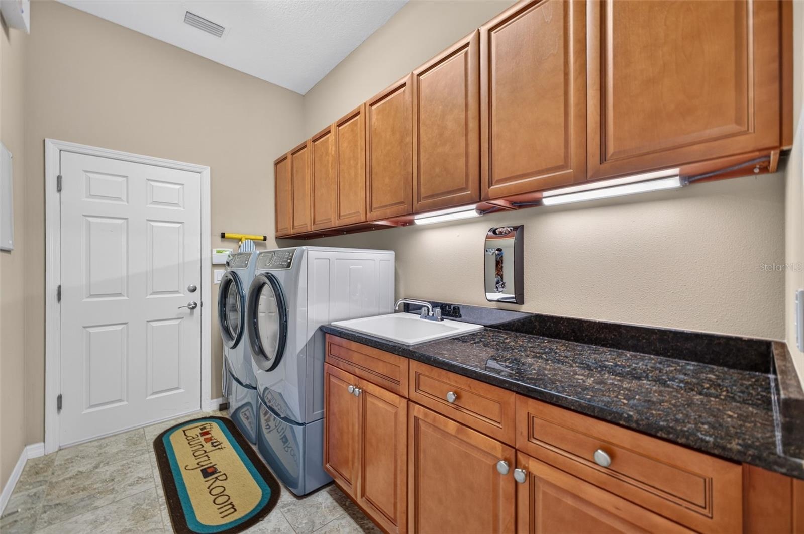 Equipped with rich granite counters, a built-in utility sink, and abundant cabinet storage, this interior laundry room doubles as a convenient drop zo