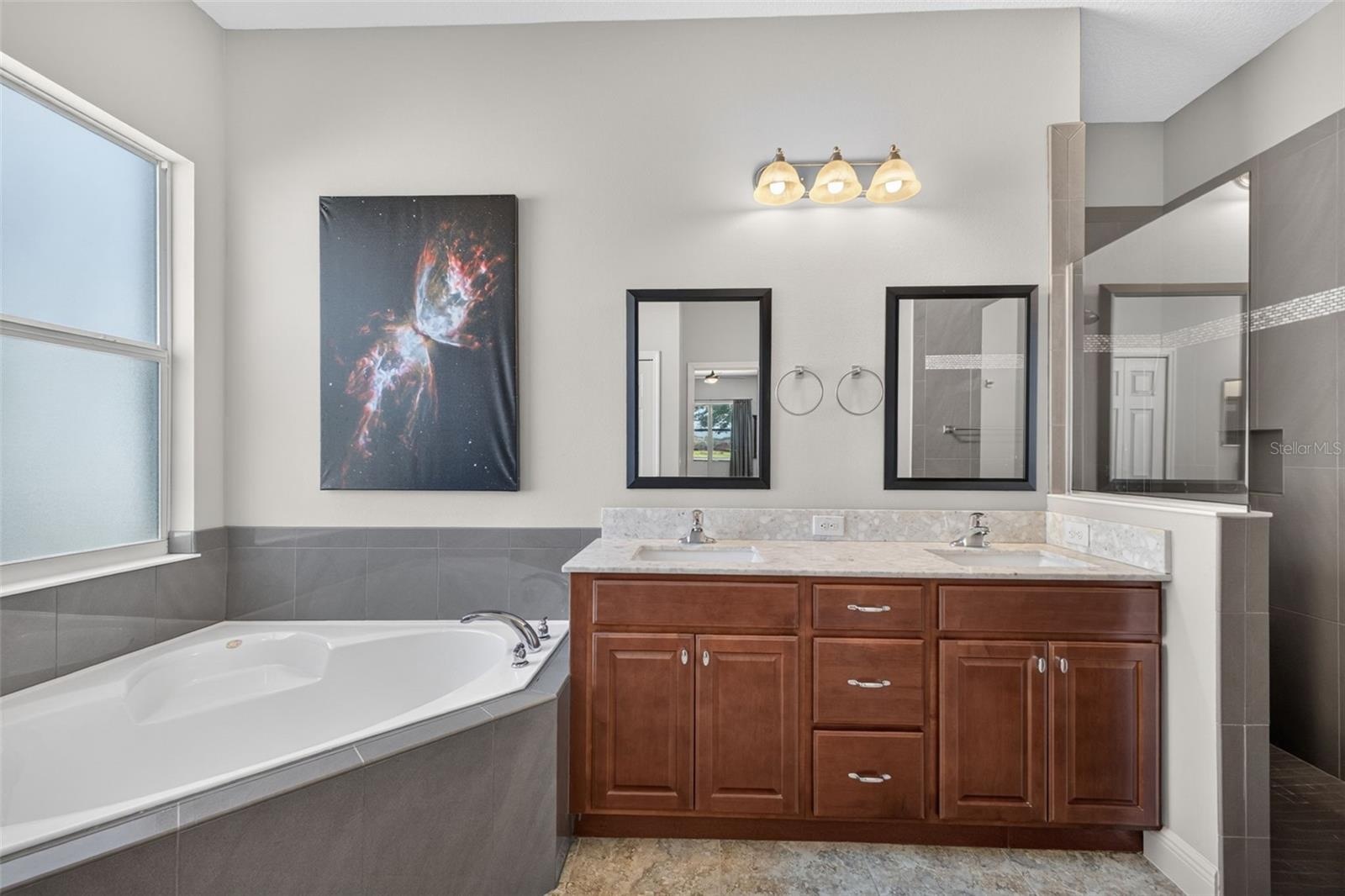 Dual vanity sinks and generous wood cabinetry provide abundant storage and counter space for effortless morning routines.