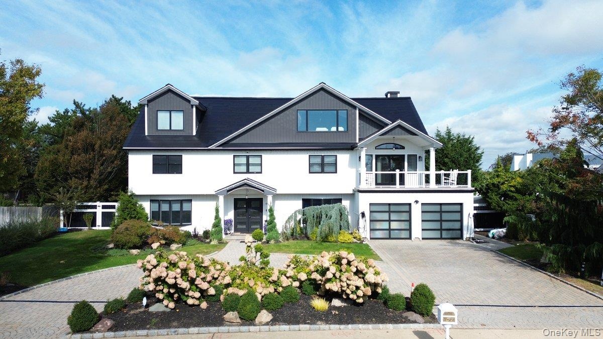 Two-story exterior featuring a high-contrast facade, dual glass-paneled garage doors, an elevated balcony, dormer windows, and a paver stone driveway