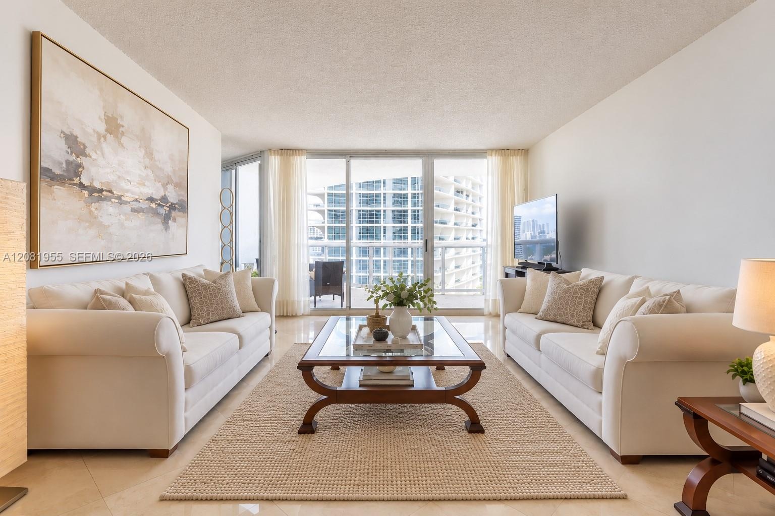Living area featuring light-toned tile flooring, floor-to-ceiling glass paneling, and an expansive sliding door leading to an outdoor balcony