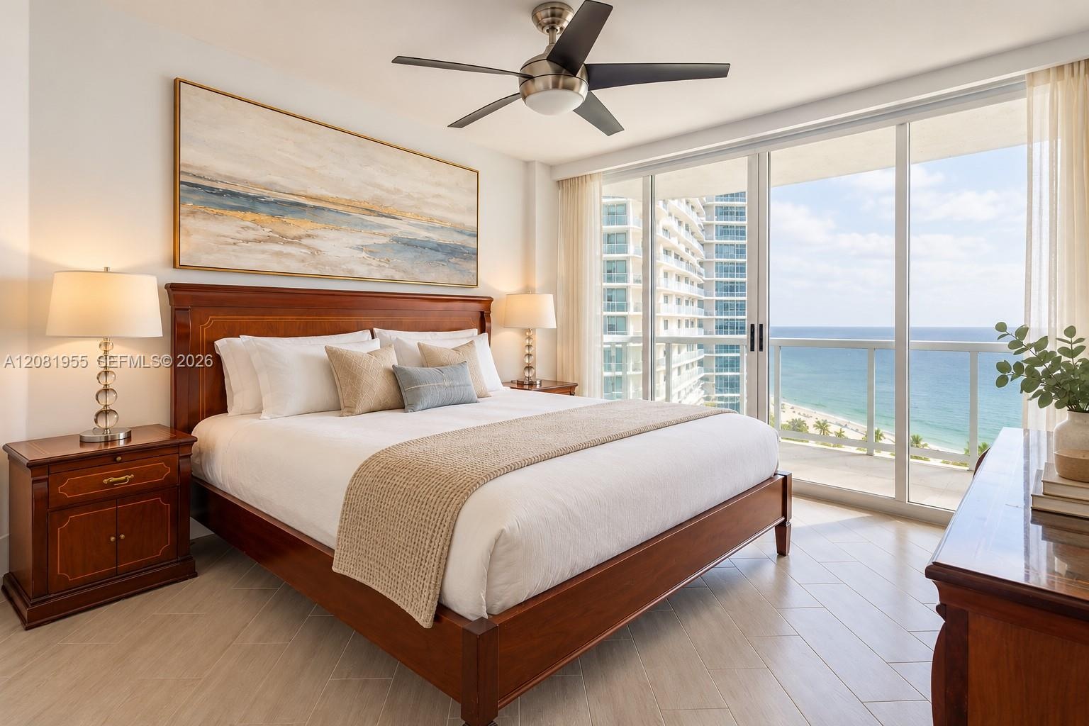 Full-height sliding glass doors with access to a balcony, light-toned wood-finish flooring, and a ceiling-mounted brushed metal fan with integrated li