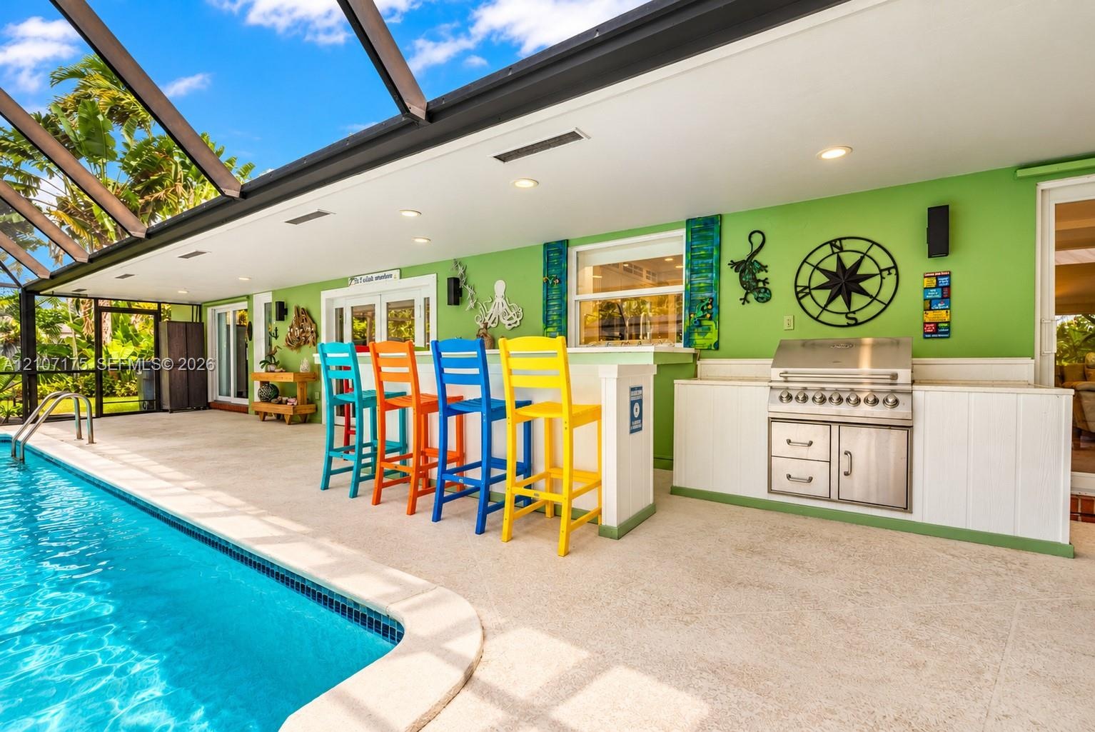 Screened lanai featuring a built-in outdoor kitchen with stainless steel grill, composite bar-height counter, recessed ceiling lighting, and pool with