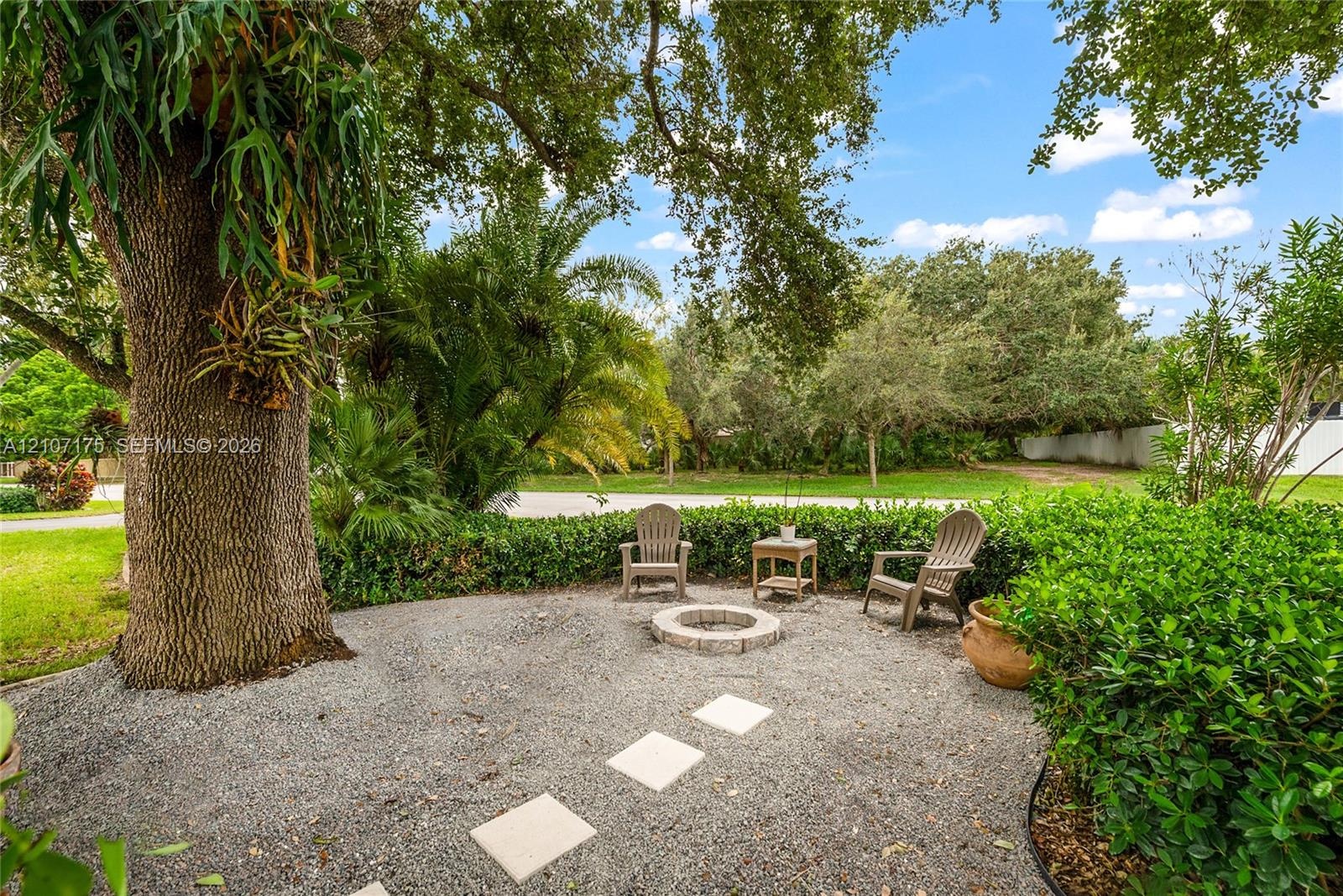 Outdoor space featuring a gravel courtyard, a circular stone fire pit, paver stones, and mature landscape elements.