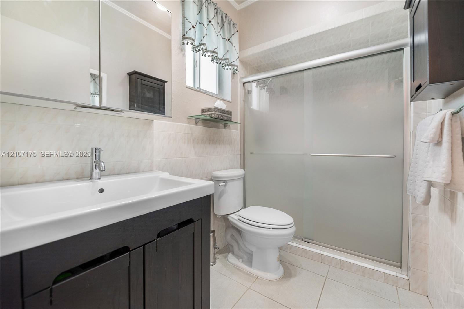 4th Bedroom En-Suite Bath. Dark wood-finish vanity with a rectangular sink, polished chrome faucet, tile-surround shower with frosted sliding glass do
