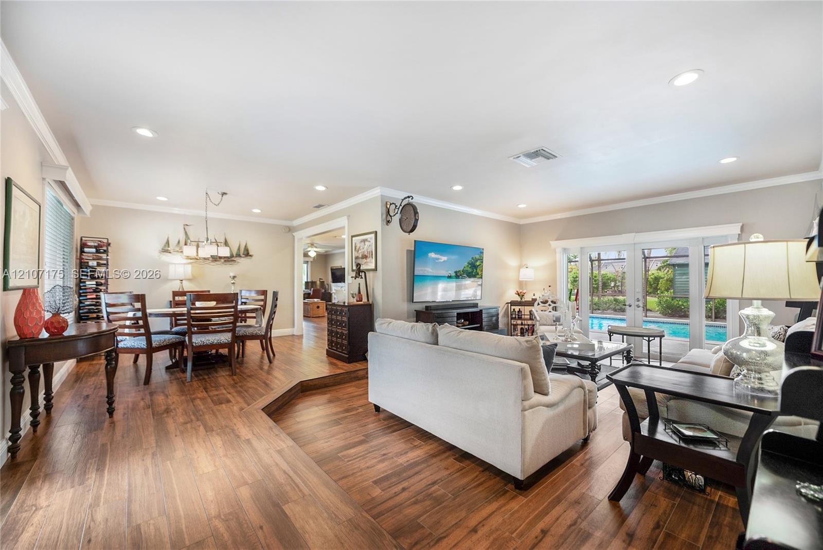 Open living room with wood-finish tile flooring, recessed lighting, crown molding, and impact glass French doors.