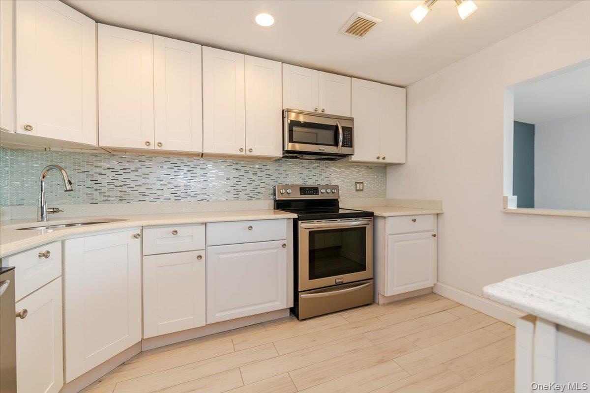 Kitchen with light countertops, white cabinets, visible vents, stainless steel appliances, and a sink