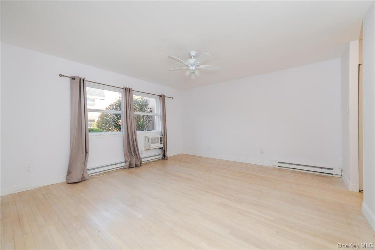 Spare room featuring a ceiling fan, baseboards, light wood-type flooring, and baseboard heating