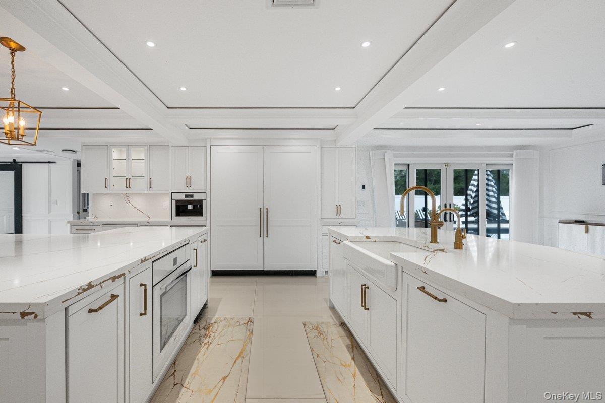 Kitchen featuring white custom cabinetry, dual islands with stone-look countertops, farmhouse-style sink, recessed lighting, and integrated panel-read
