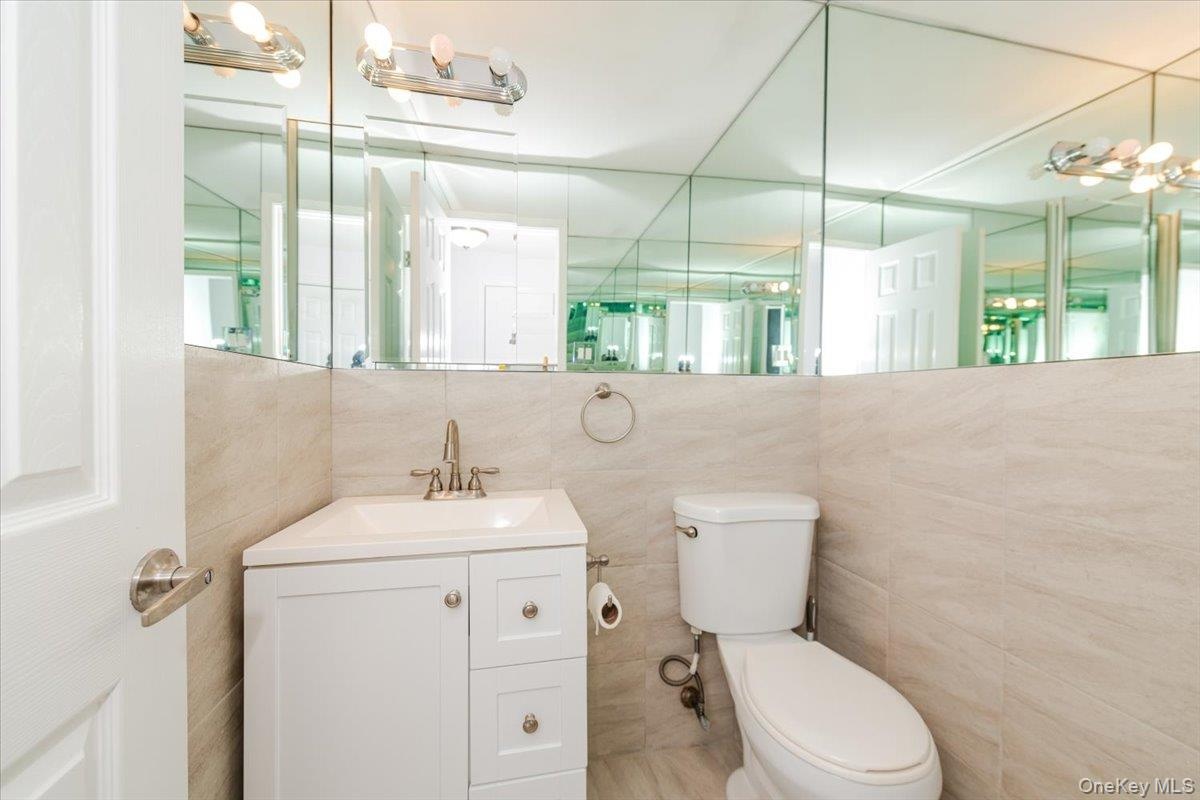 Bathroom featuring toilet, vanity, and tile walls