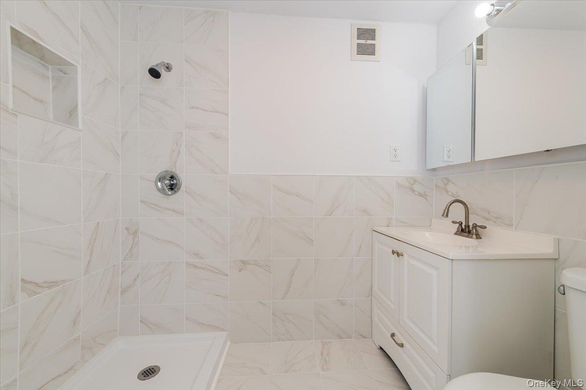 Bathroom featuring tiled shower, vanity, visible vents, and toilet