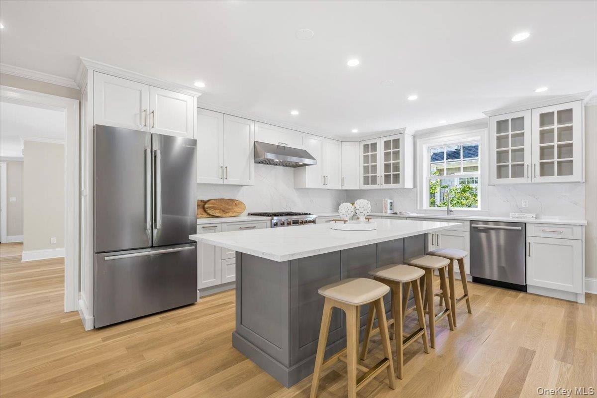 Kitchen features oversized island with Quartz countertops and backsplash, custom cabinets with wood insert details, Bosch appliances.