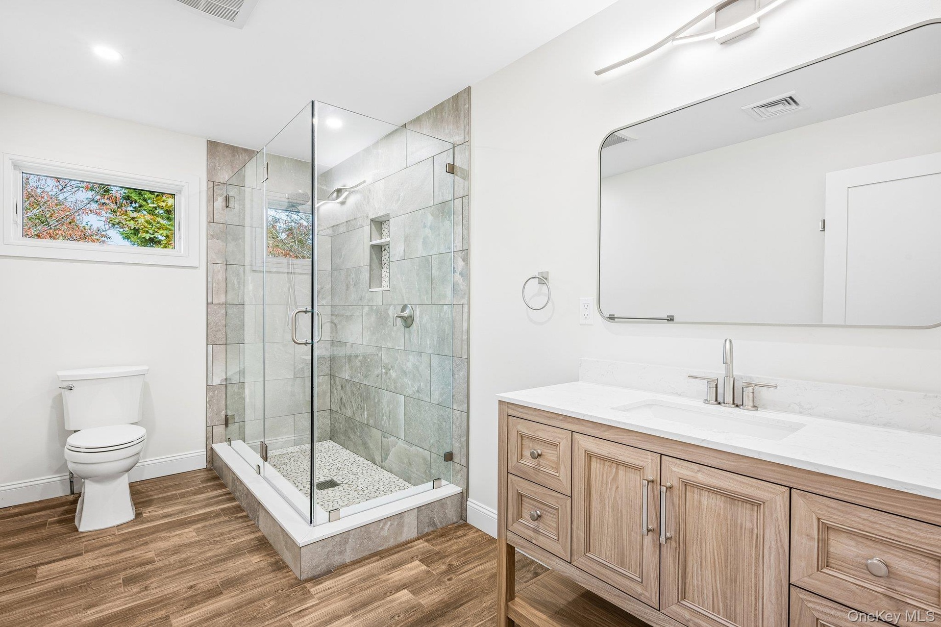 A full bath with glass shower and warm wood vanity. Tomorrow's plan: the Eggs Amsterdam at JT's Cafe on Montauk Highway, under a mile away, then a lap